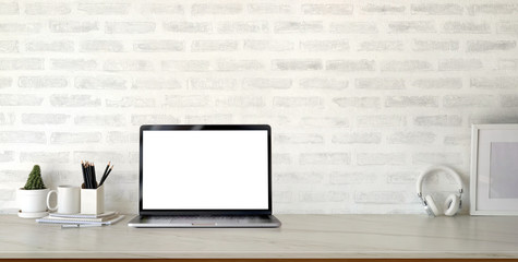 Cropped shot of modern stylish workplace with open blank screen laptop computer and office supplies on marble desk and brick wall