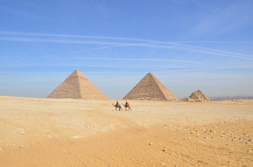 Tourists riding camel exploring the Giza Plateau with the Pyramids around.