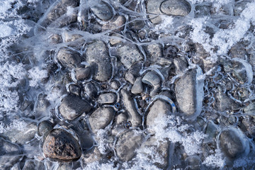 Natural winter background of frozen pebbles and hoarfrost crystals over river ice
