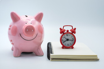 Pink piggy bank Red alarm clock And expense book White background. Concept of revenue collection Savings by accounting for investments, retirement funds.Timing in the financial period.
