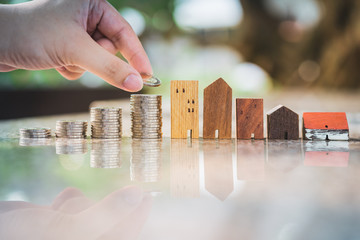 Hand choosing row of coin money on wood table and mini wood house, selective focus, Planning to buy...