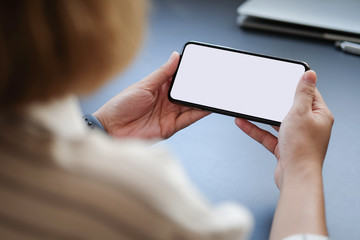 Cropped shot view of woman hands holding smart phone with blank copy space screen for your text message or information content, female reading text message on cell telephone during in urban setting. 