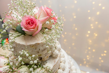 Close up of beautiful white tree tier cake with fresh flowers with fairly light and lanterns glowing in the background on a wooden rustic table. Selective focus. Copy space.