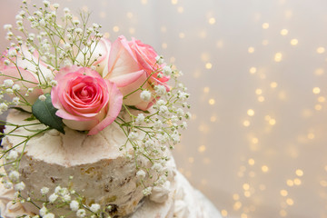 Close up of beautiful white tree tier cake with fresh flowers with fairly light and lanterns glowing in the background on a wooden rustic table. Selective focus. Copy space.