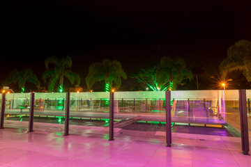 Long exposure of a palm-fringed pool area in the background with spiraling green lights on its logs.