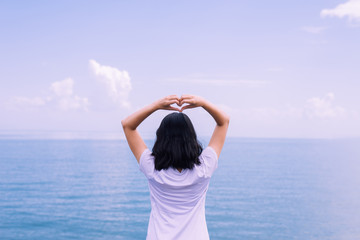 Happy young asian woman standing and showing 2 fingers at sea,Enjoying in Nature,Freedom concept,Back view