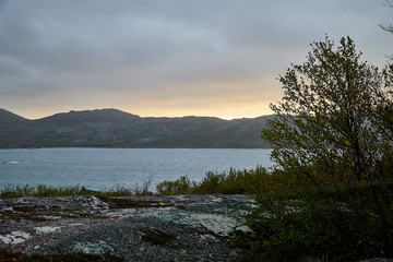 Car on the beach of sea, river or lake with rocks on a cloudy day. The fjord of Northern Norway