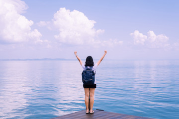 Happy young asian woman standing with hand raise up at sea,Enjoying in Nature,Freedom concept,Back view