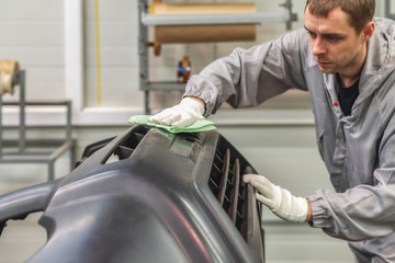 An employee of the paint shop of the automobile plant removes dust with a wax rag and prepares the...