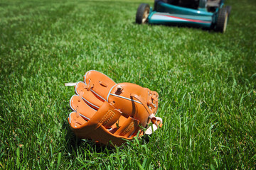 Lawnmower in backyard about to run over a baseball glove laying in the grass