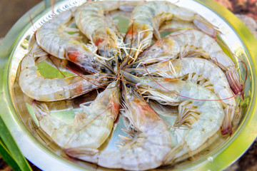 Freshly caught shrimp on a round iron platter, close-up. King prawns in a shell before cooking. Seafood restaurant.