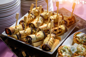 Eggplant appetizer on crispy toast, close-up. Baked eggplant in rolls on a wooden skewer. Cold snacks at banquet.