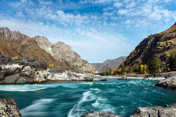 Fototapeta na wymiar Wide river flows along stony banks among rocky mountains against clear blue sky. Turquoise water of stormy river and huge stones. Stunning natural background.