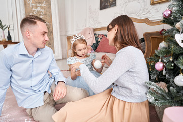 Obraz na płótnie Canvas Loving family. Mom and dad hugging little daughter . Parents and baby child having fun near Christmas tree and white fireplace indoors. Merry Christmas and Happy New Year. Cheerful pretty people.