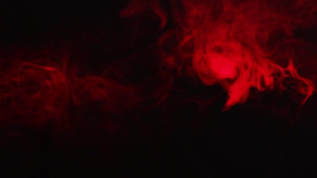 Red smoke swirls and changes color on black isolated background . A cloud of smoke moves in a chaotic manner