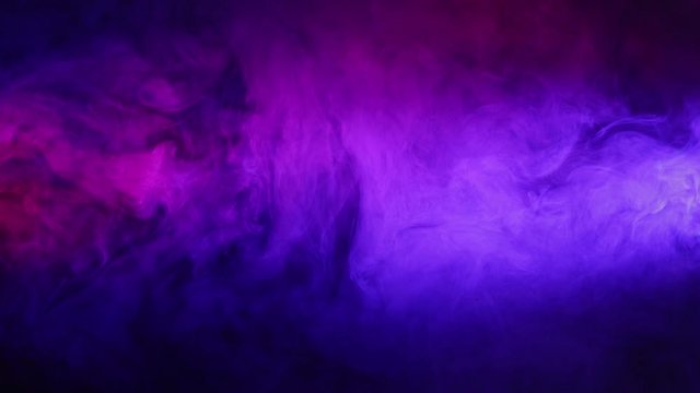 Purple, pink and blue  smoke swirls and changes color on black isolated background . A cloud of smoke moves in a chaotic manner