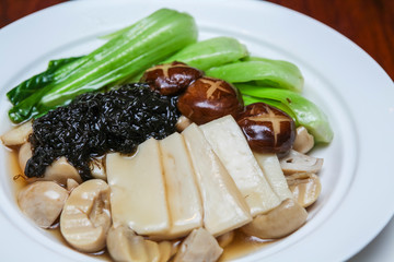 Stir-fried seaweed, bamboo shoots, mushrooms and vegetables. Vegetarian food In a white plate on a wooden table.