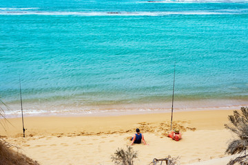 Fototapeta na wymiar Two man relaxing on a beach with fishing rods.