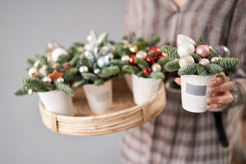 Florist holds a tray with christmas arrangements and one in his hand. Beautiful festive arrangement of fresh spruce in coffee Cup. Christmas mood.