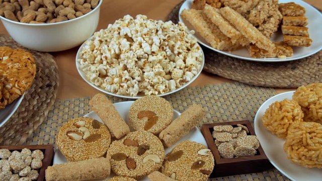 Pan shot of different Lohri items consumed during the Punjabi's Lohri festival in India. Closeup shot of beautifully plated murmura ladoos  peanuts chikki  murmura chikki  popcorn  rewri  groundnut...