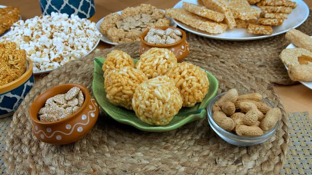 Beautifully placed delicious Lohri items rotating on a turntable - Punjabi's Lohri festival. Closeup shot of murmura ladoo  rewri  and groundnuts surrounded by bhujia chikki  popcorns  gajak  peanu...