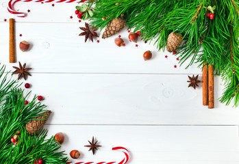 Fototapeta na wymiar Christmas fir tree and heather decoration, fir cones and red berries of cranberry, cinnamon sticks and star anise spices, hazelnuts on a white wooden background. Christmas greeting card. Text space.