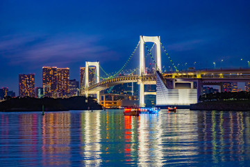Naklejka premium Japan. The Island Of Odaiba. Rainbow bridge in the evening. Travel to the artificial Islands of Japan. A trip to the island of Odaiba. Pacific Bay. Suspension bridge on the background of buildings.