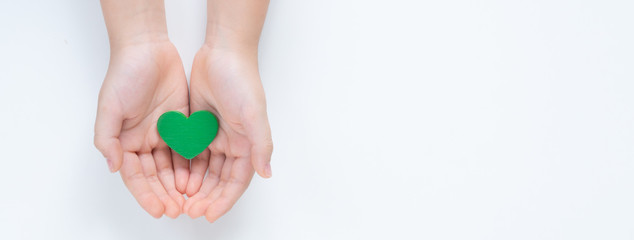 Hands of a young child holding a beautiful green heart with care showing a concept of Environmental friendly, Sustainable living, Eco day, Clean energy, Vegan. Isolated top view on white background