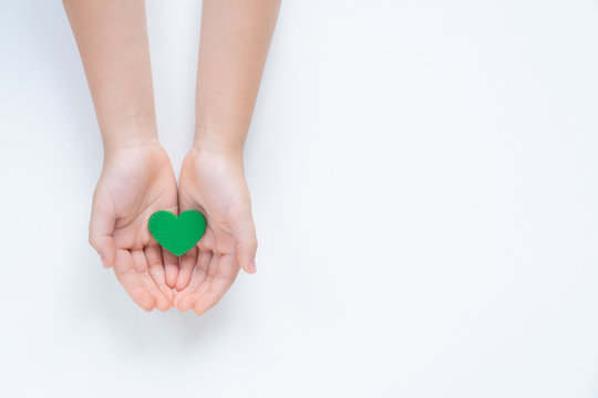 Hands of a young child holding a beautiful green heart with care showing a concept of Environmental friendly, Sustainable living, Eco day, Clean energy, Vegan. Isolated top view on white background