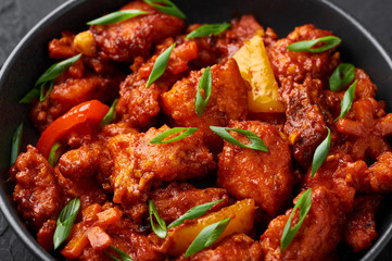 Fish Manchurian dry looks like Schezwan Fish in black bowl at dark slate background. Fish Manchurian - is indo chinese cuisine dish with deep fried salmon, bell peppers, sauce and onion.