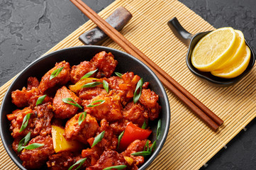 Fish Manchurian dry looks like Schezwan Fish in black bowl at dark slate background. Fish Manchurian - is indo chinese cuisine dish with deep fried salmon, bell peppers, sauce and onion.