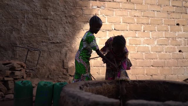 Two Joyful Girls At The Village Well Pulling Up Together A Heavy Water Bucket 