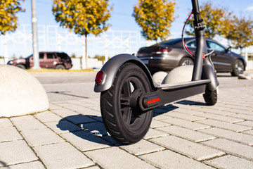 Close up view of e-scooter parked on sidewalk at cityscape on the sunset. Trendy urban...