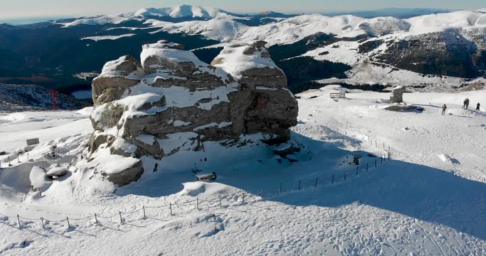 Aerial, orbit, drone shot around the sphinx rock formation, on the top of the southern Carpathians, on a sunny winter day, in the Bucegi Natural Park, Romania