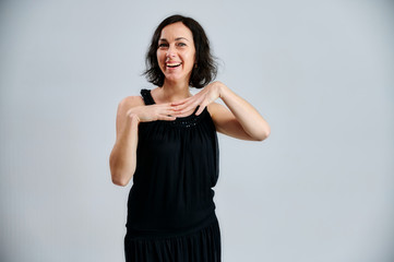 Portrait of a pretty brunette woman in a black dress on a white background. Shows emotions with hands in different poses right in front of the camera.