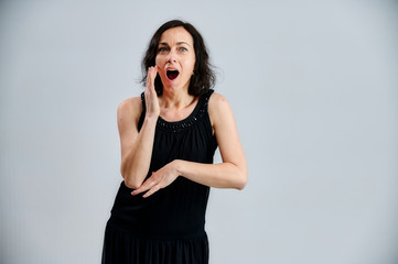 Portrait of a pretty brunette woman in a black dress on a white background. Shows emotions with hands in different poses right in front of the camera.