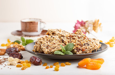 Homemade granola from oat flakes, dates, dried apricots, raisins, nuts in blue ceramic plate on a white wooden background. Side view, selective focus.