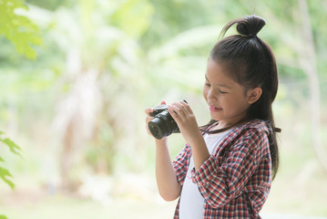 Girl who takes pictures with a photo camera in park on Green natural background. Beautiful smiling child holding a instant camera.