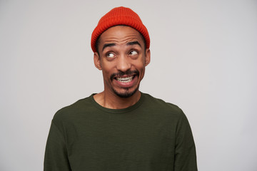 Cheerful young lovely dark skinned brunette man with beard showing his white perfect teeth while grimacing to camera, posing over white background in casual wear