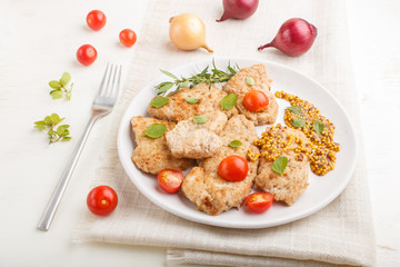 Fried pork chops with tomatoes and herbs on a white ceramic plate on a white wooden background. side view, close up.
