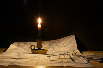 La cartina sulla tavola illuminata dalla fiamma della candela - obrazy, fototapety, plakaty
