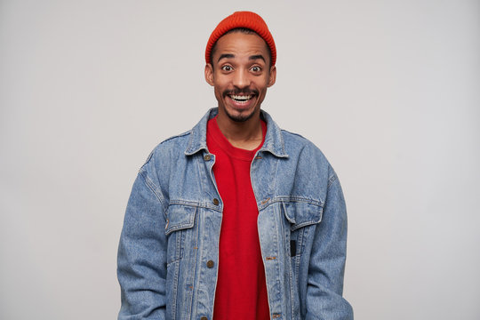 Studio photo of joyful young bearded dark skinned brunette guy in casual clothes raising surprisedly eyebrows while looking at camera with wide eyes and mouth opened, isolated over white background
