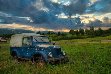 Obraz na płótnie Canvas Old car wreck on meadow with dramatic sky