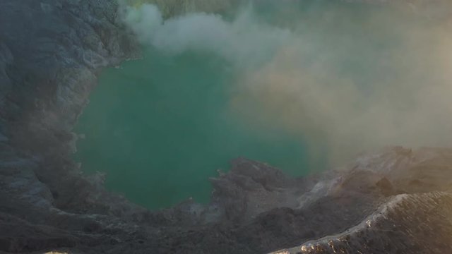 Aerial Pan Up of Acidic Lake With Smoke Inside a Volcano Reavealing Mountainous Landscape in Background