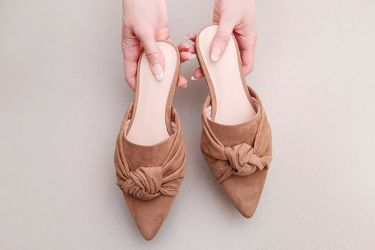 Woman holds a pair of beige mule shoes.