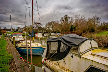 Fototapeta na wymiar Derelict and wrecked motor boats and cruisers moored up in a dyke off the Norfolk Broads on a dull and overcast day