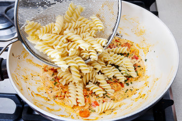 The cook mixes the pasta with a thick sauce and vegetables.