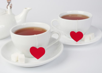 Two white cups of tea with tea labels in the form of red hearts. Light background.
