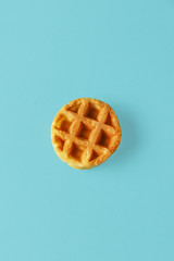 Small round Belgian waffle on trendy blue background. Minimal food and bakery concept, modern and contemporary style, top view and close up
