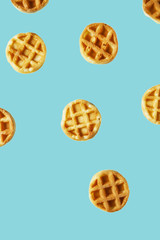 Flying small round waffles isolated on trendy blue background. Minimal food and bakery concept, modern and contemporary style